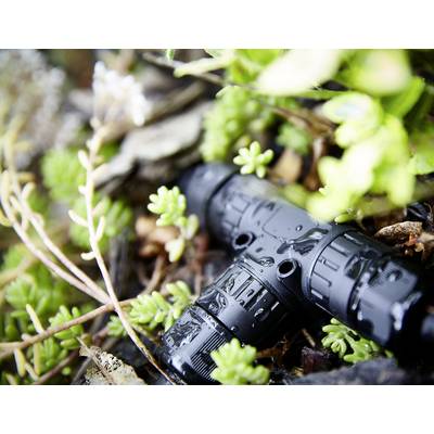 Un objet noir et cylindrique est posé entre des plantes et des feuilles vertes. Il est mouillé et se trouve à l'extérieur.