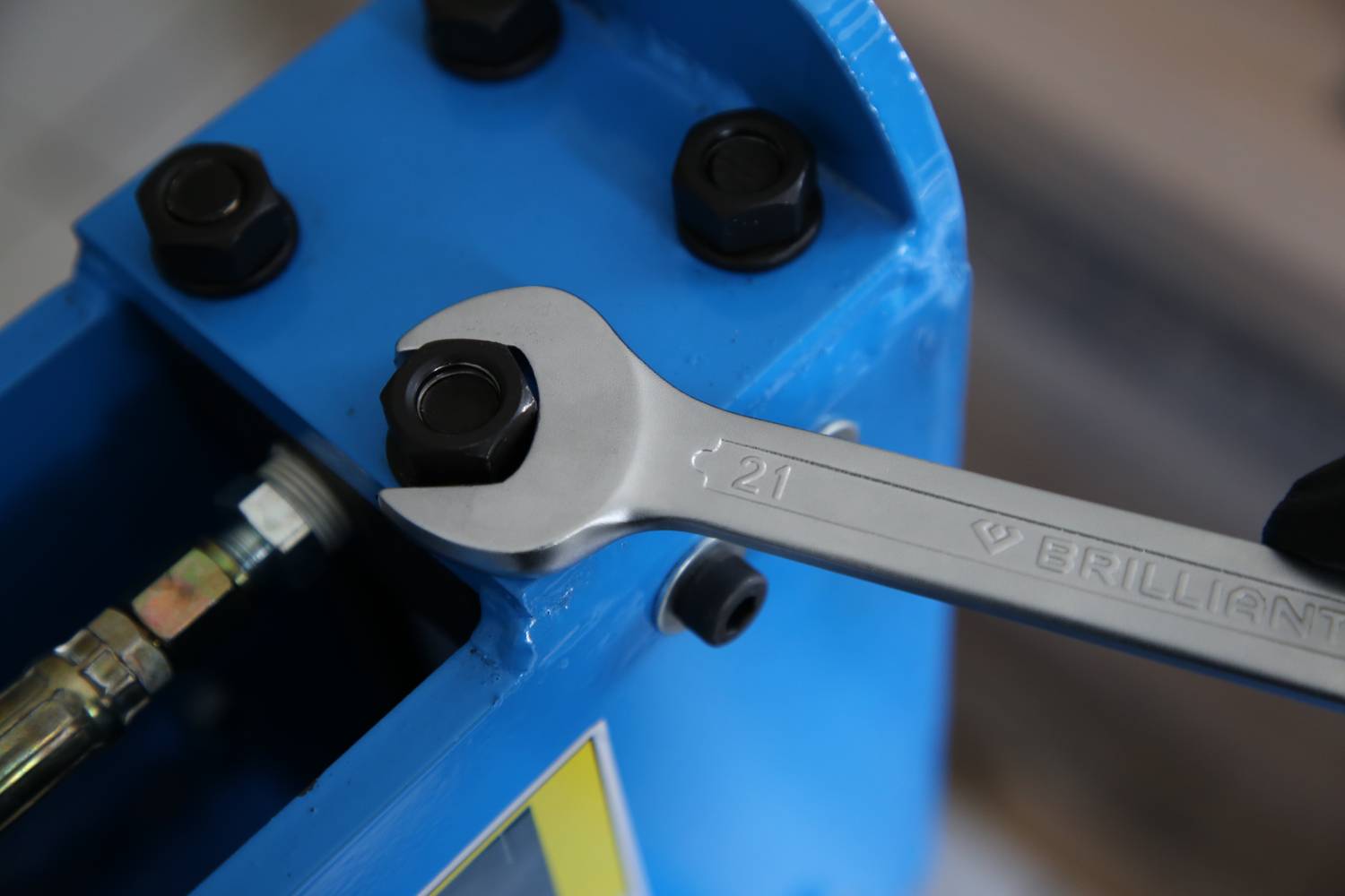 Une clé à molette serre un écrou sur une machine métallique bleue. La clé porte l'inscription « 21 Brilliant ».