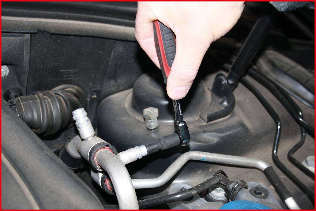 Quelqu'un répare un moteur de véhicule avec une clé à molette en serrant un tuyau.