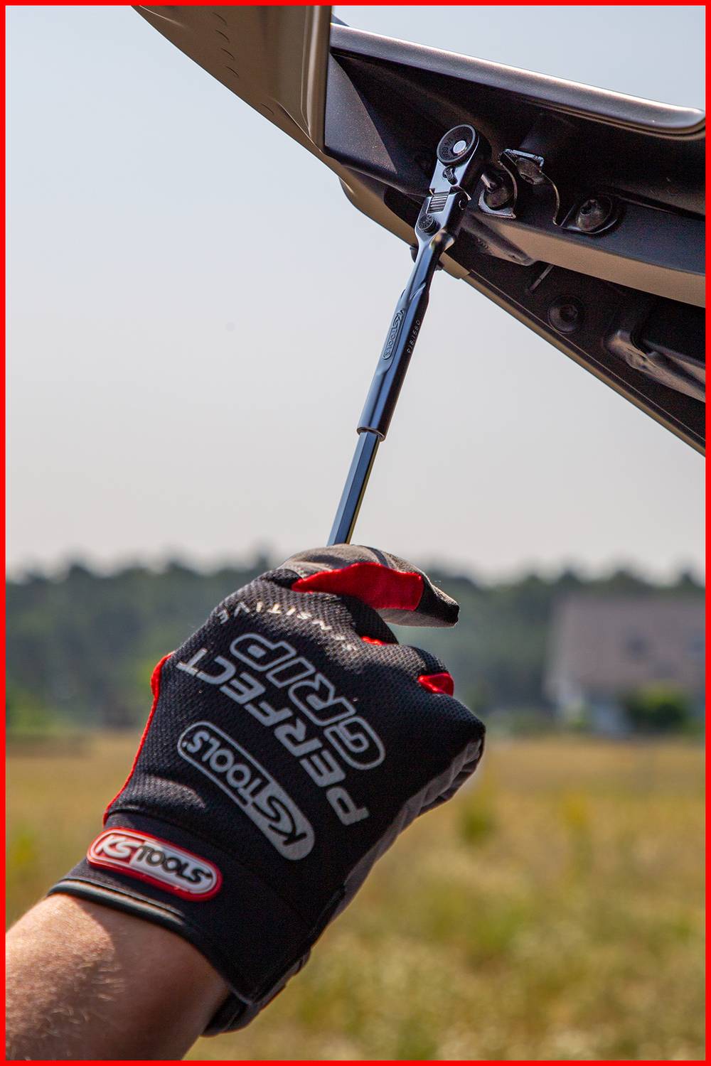 Une personne portant des gants serre une vis à l'aide d'un outil à cliquet ; un paysage est visible en arrière-plan.