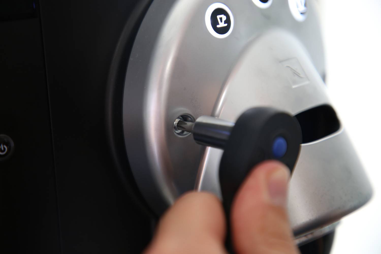 Une main insère une clé dans la serrure d'une machine à café. La machine dispose de touches avec des symboles de tasses à café.