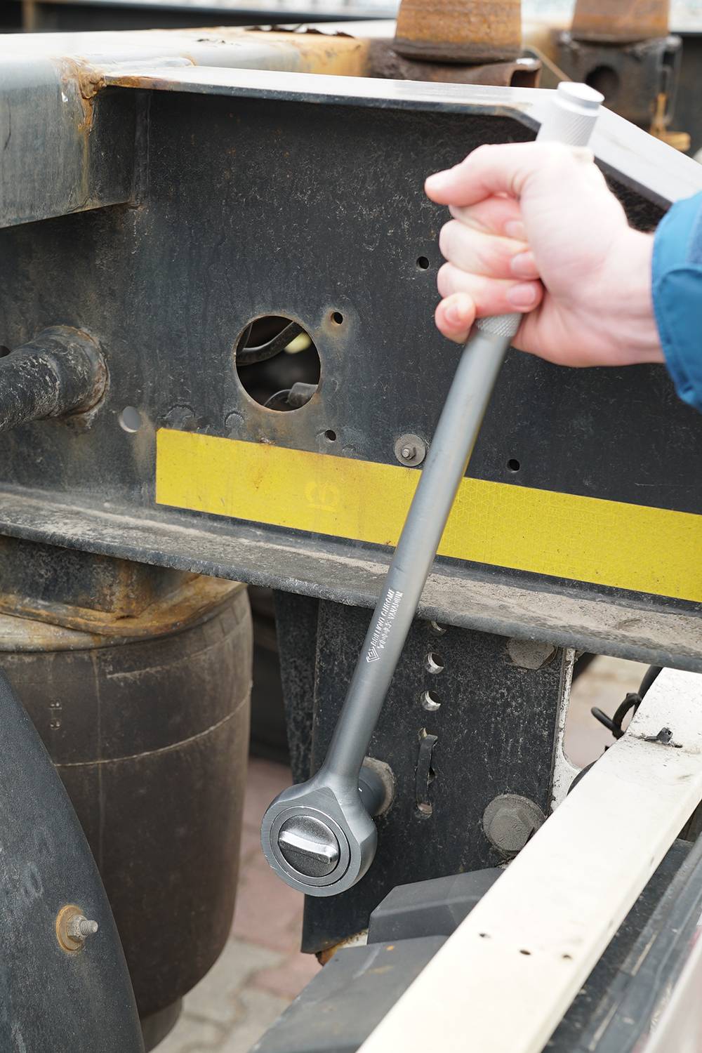 Une main tient une grande clé à molette et serre un écrou sur un cadre métallique industriel.