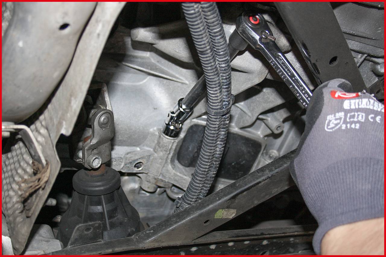 Un mécanicien serre une vis sur le moteur d'une voiture à l'aide d'une clé dynamométrique. Des câbles et des pièces du véhicule sont visibles.
