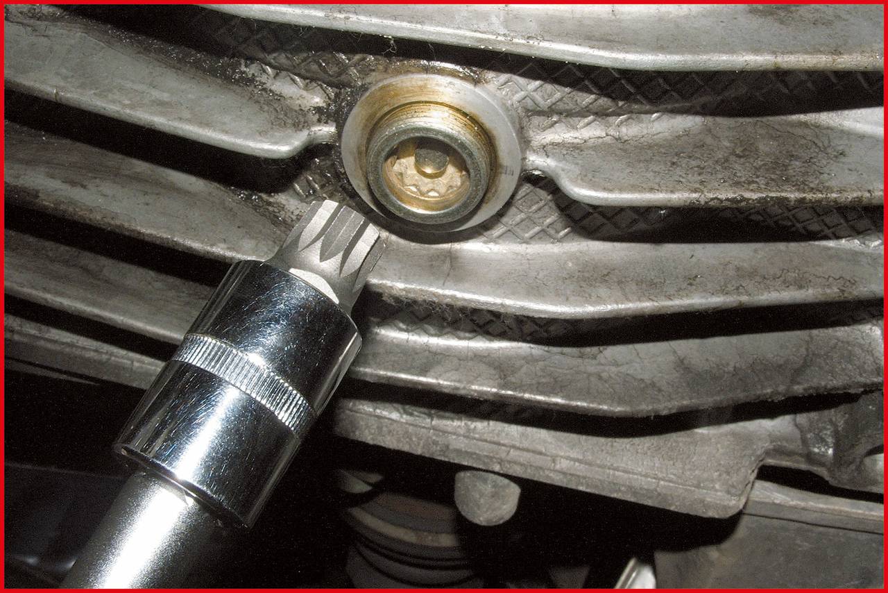 Une clé à molette est fixée à une vis sous un véhicule, probablement pour des travaux de maintenance ou de réparation.