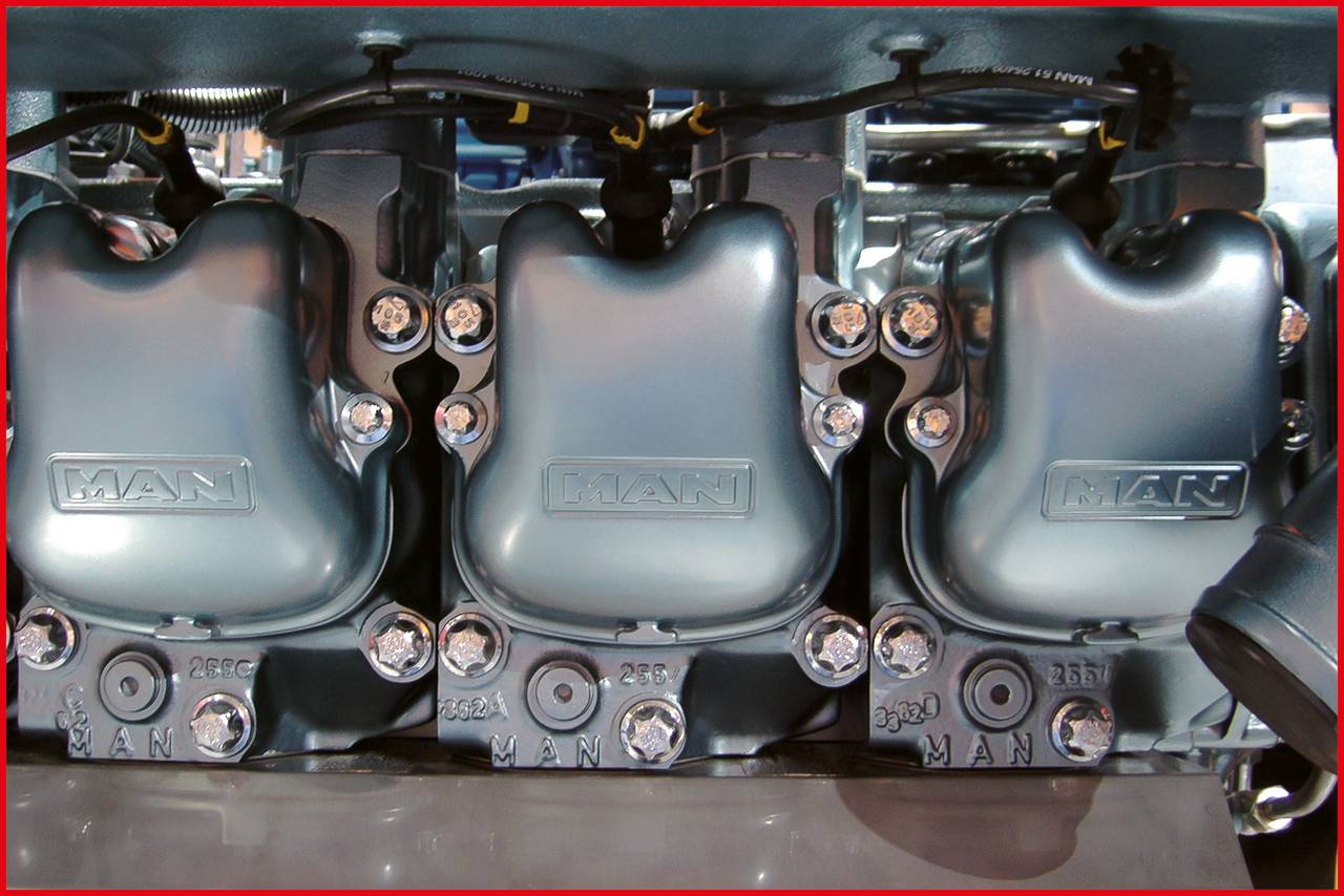 Gros plan d'un moteur de machine industrielle avec trois boîtiers métalliques, sur lesquels est gravé 'MAN'. Des détails mécaniques sont visibles.