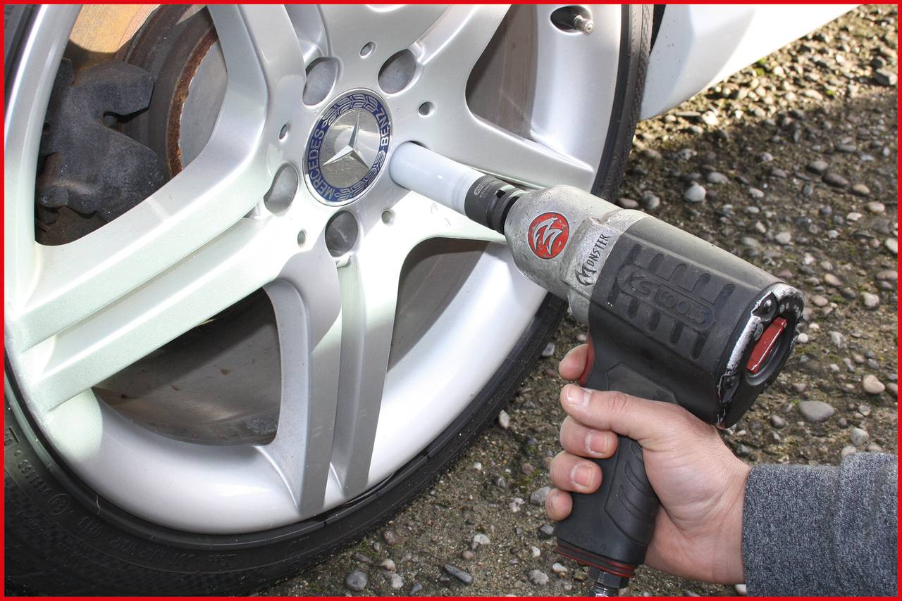 Une main utilise une visseuse à choc pour serrer les écrous de roue d'un pneu de voiture à jante argentée.
