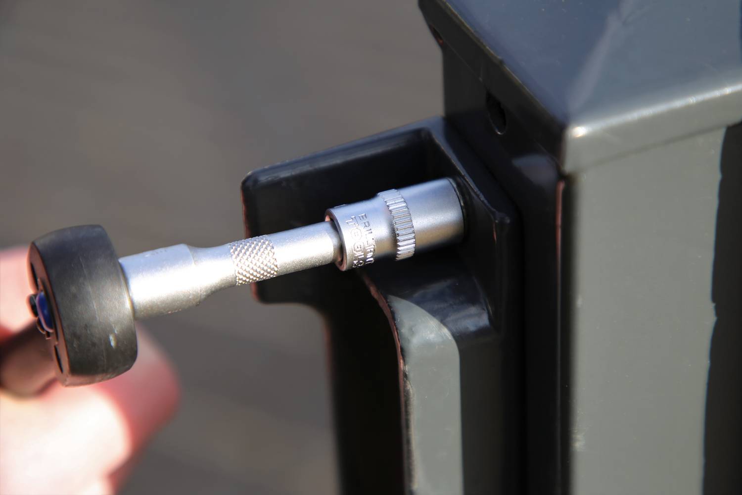 Une main utilise une clé Allen pour serrer une vis sur un poteau métallique de portail.