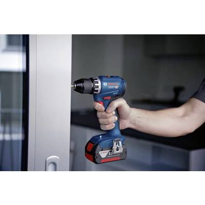 Une personne tenant une perceuse électrique sans fil près d'une fenêtre, suggérant des activités de rénovation ou de réparation à domicile.