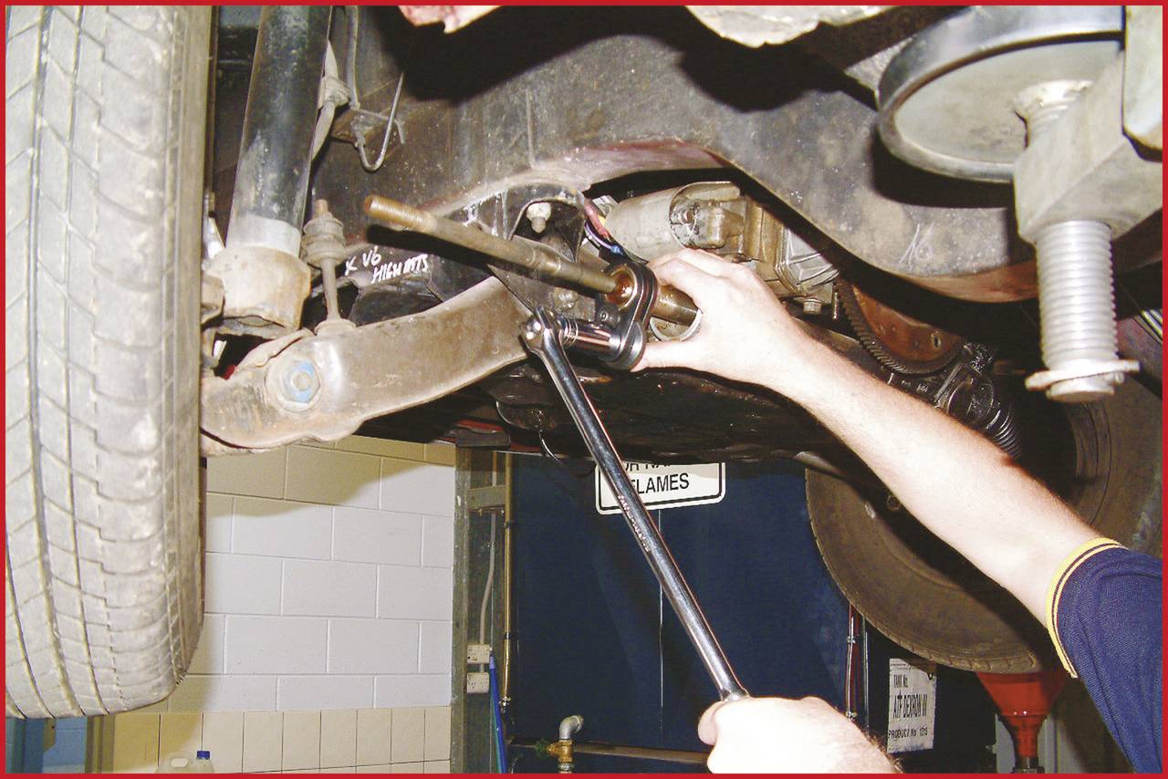Une personne répare une partie de la suspension d'un véhicule avec une clé à molette dans un atelier automobile.