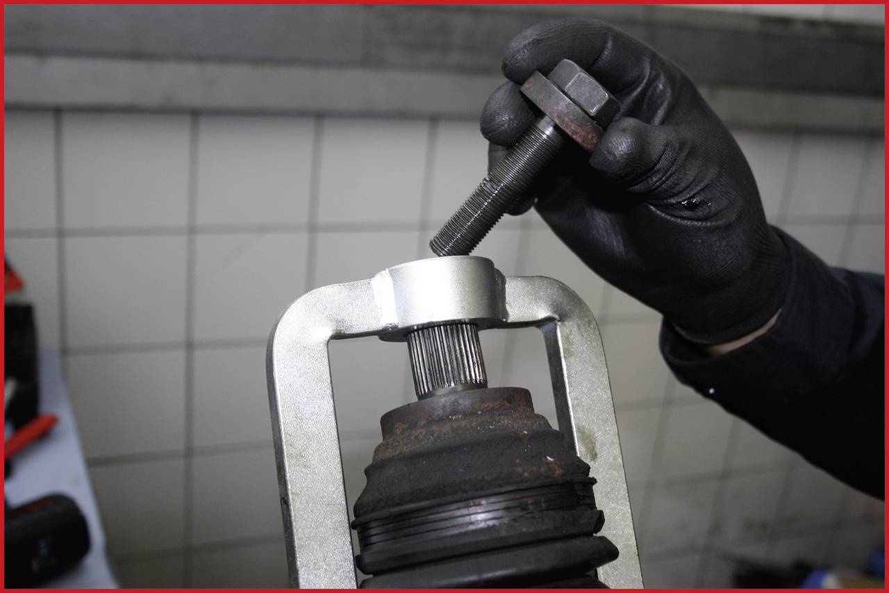 Une personne portant des gants noirs utilise un outil sur une pièce automobile dans un environnement d'atelier.