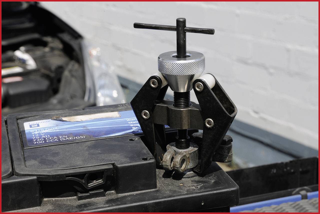 Un outil retire une borne de batterie d'une batterie de voiture. La batterie est placée dans un compartiment moteur ouvert.