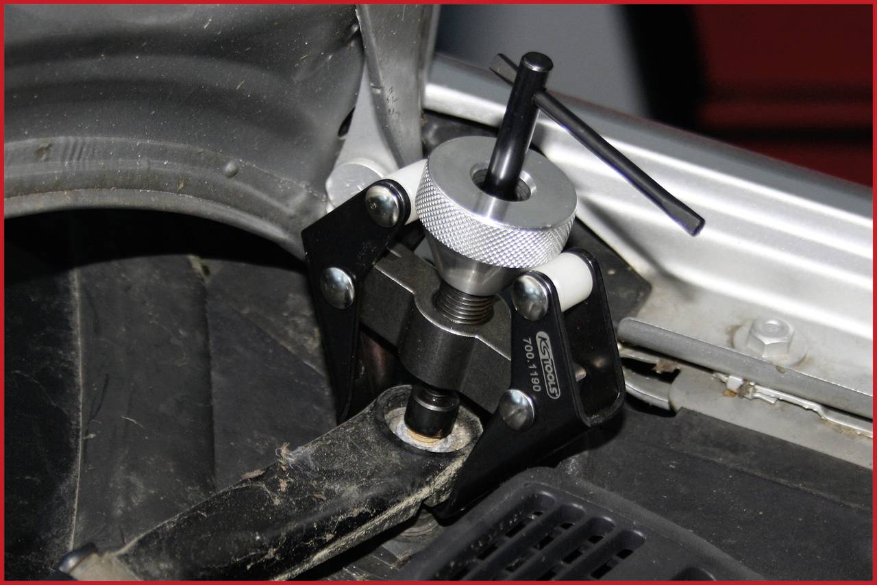 Un extracteur de rotule sur un train de suspension automobile, qui aide à démonter une rotule. Une partie du train de suspension est visible à gauche.