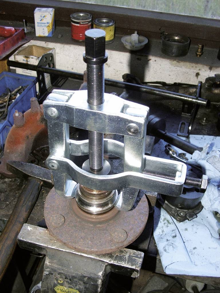 Un extracteur est utilisé pour retirer un roulement de roue d'un moyeu. La scène montre un atelier avec divers outils.
