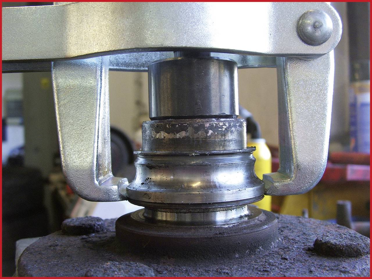 Gros plan sur un composant de machine hydraulique usinant des pièces métalliques. Un cylindre exerce une pression sur un roulement. Atelier en arrière-plan.