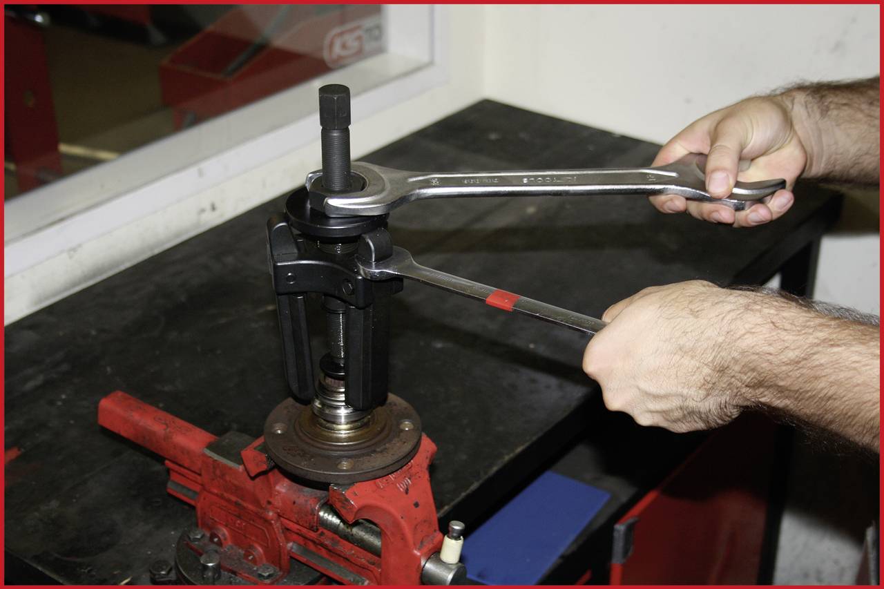 Des mains utilisent deux clés à molette pour régler ou réparer une pièce automobile dans un atelier. Étau fixé sur l'établi.