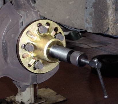Extracteur de moyeu monté sur un roulement de roue, prêt à démonter le roulement. Outils et voiture visibles dans l'environnement d'un atelier.