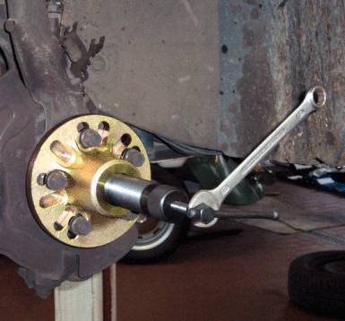 Un roulement de roue d'un essieu de voiture est fixé à l'aide d'une clé à molette. En arrière-plan, des outils sont visibles sur un établi.
