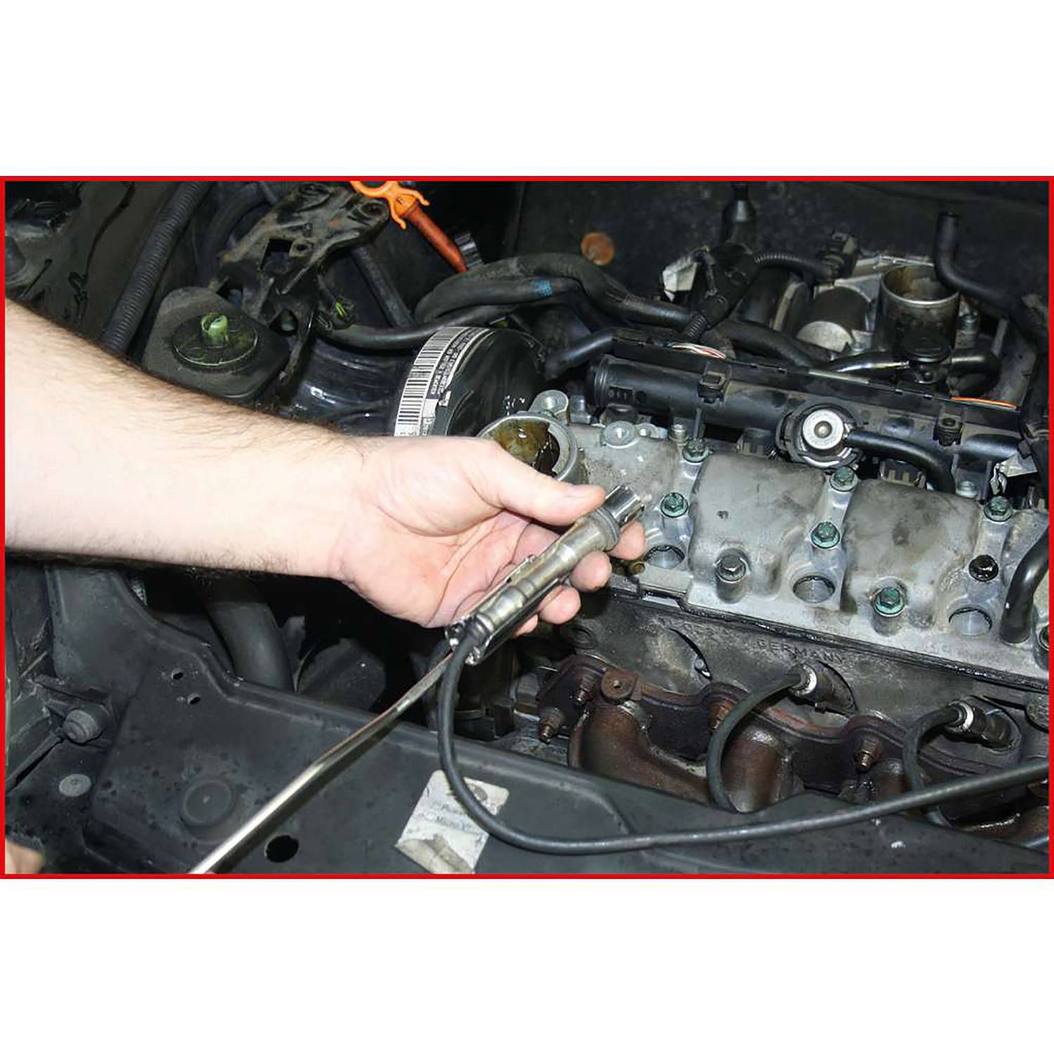 Une personne tient une sonde lambda dans sa main devant un bloc-moteur. La sonde est importante pour la mesure des émissions de gaz d'échappement dans une voiture.