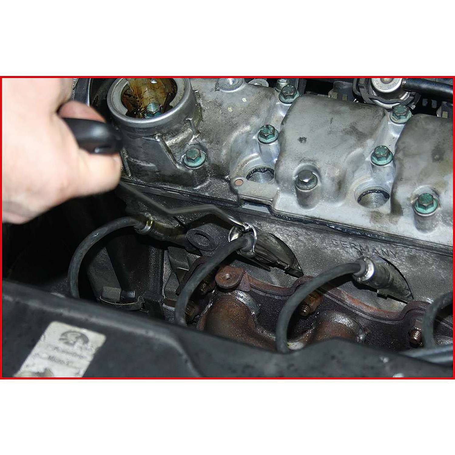 Un mécanicien retire un câble de bougie d'allumage de la culasse d'une voiture. On peut voir des traces d'usure et d'huile dans le moteur.