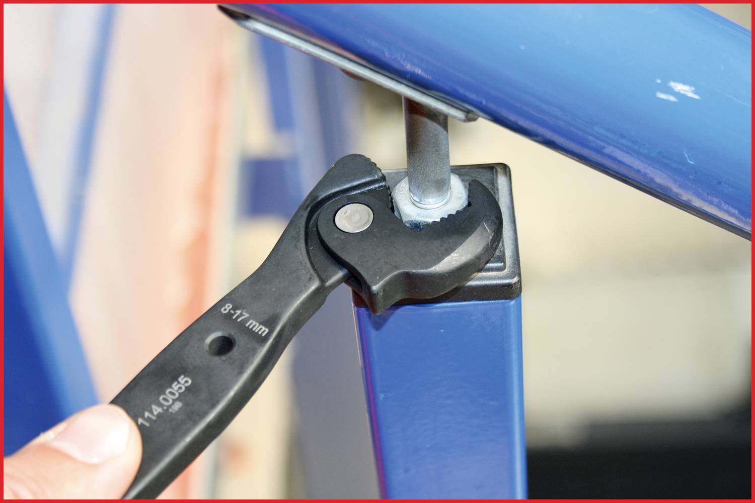 Une main tient une clé à molette qui serre un écrou sur une structure métallique bleue.