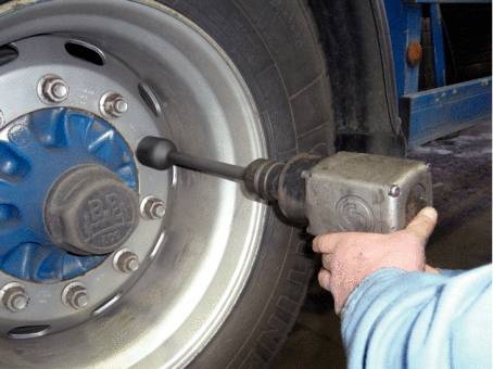 Une personne serre les écrous de roue d'un pneu de camion à l'aide d'une visseuse à chocs. Environnement d'atelier en arrière-plan.