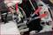 Une personne utilise deux pinces rouges pour travailler sur une pièce automobile. Le compartiment moteur et les tuyaux sont visibles.