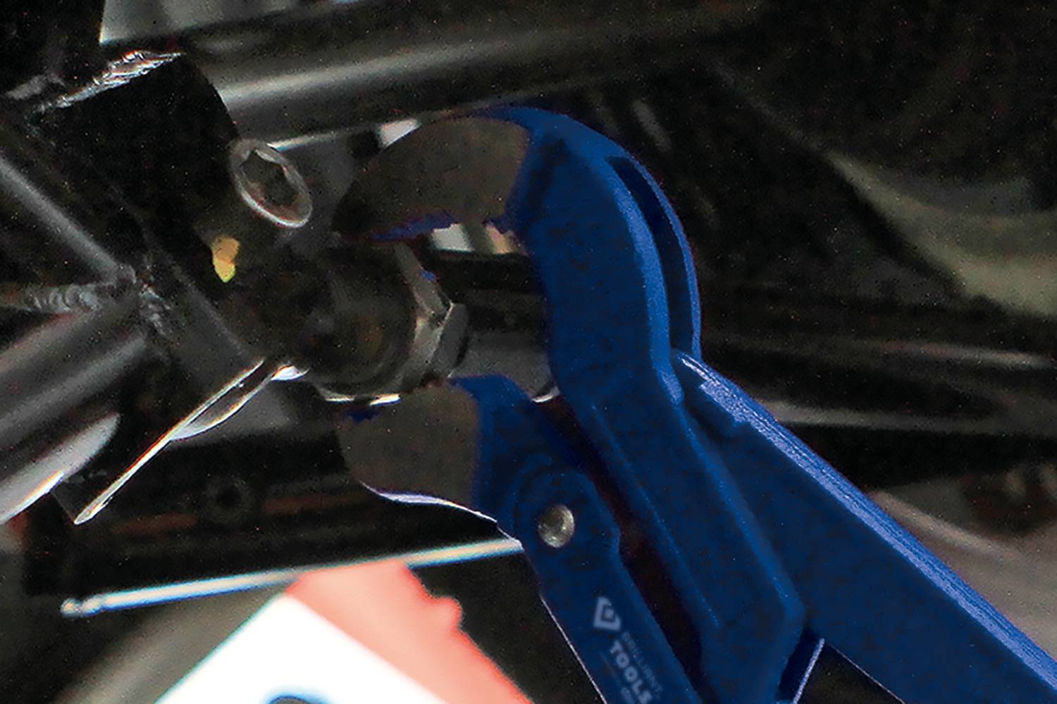 Une pince bleue serre un boulon sur un bâti métallique.