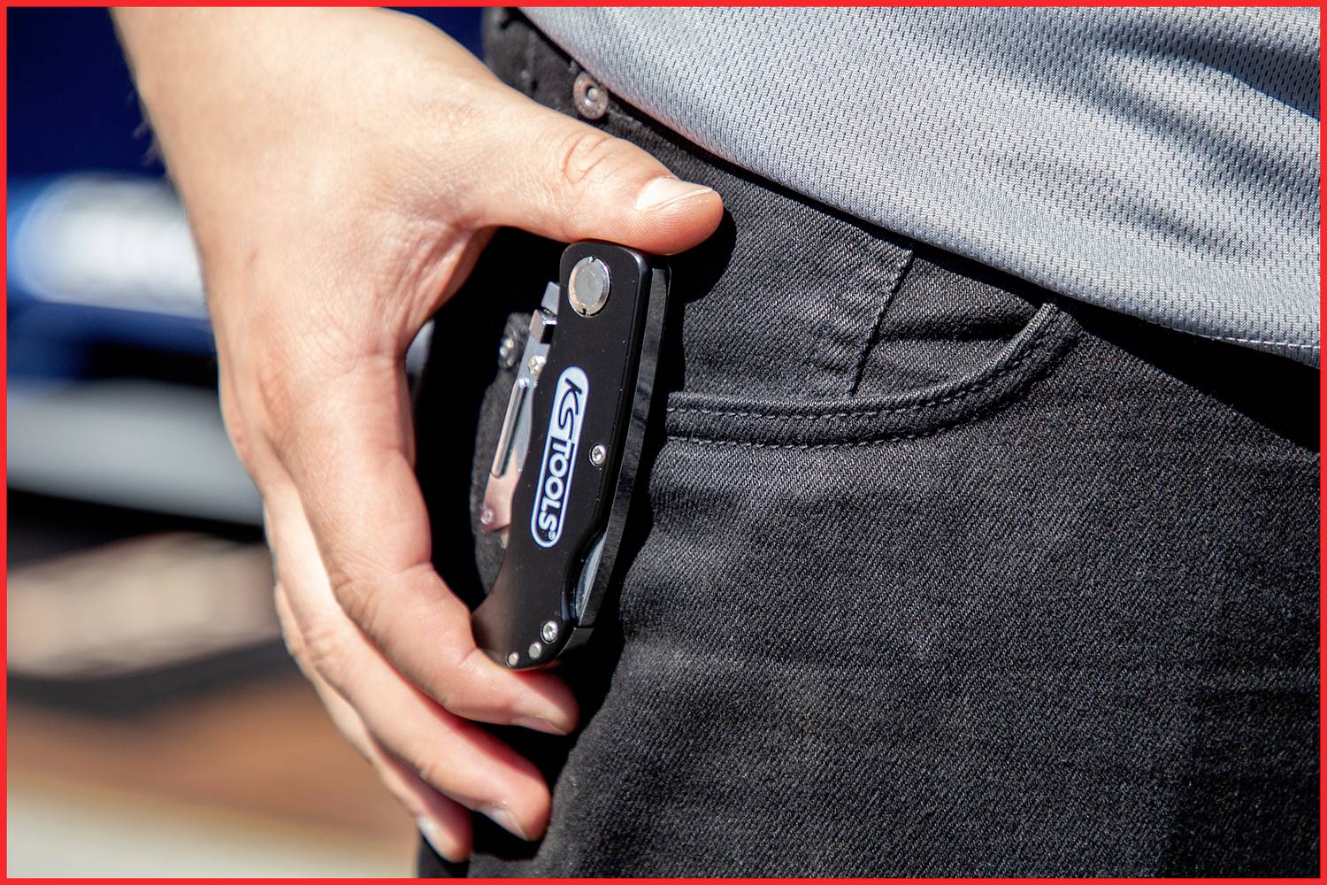 Une personne tend la main droite vers un couteau pliant dans sa poche de pantalon. Le couteau porte l'inscription 'STOOLY'.