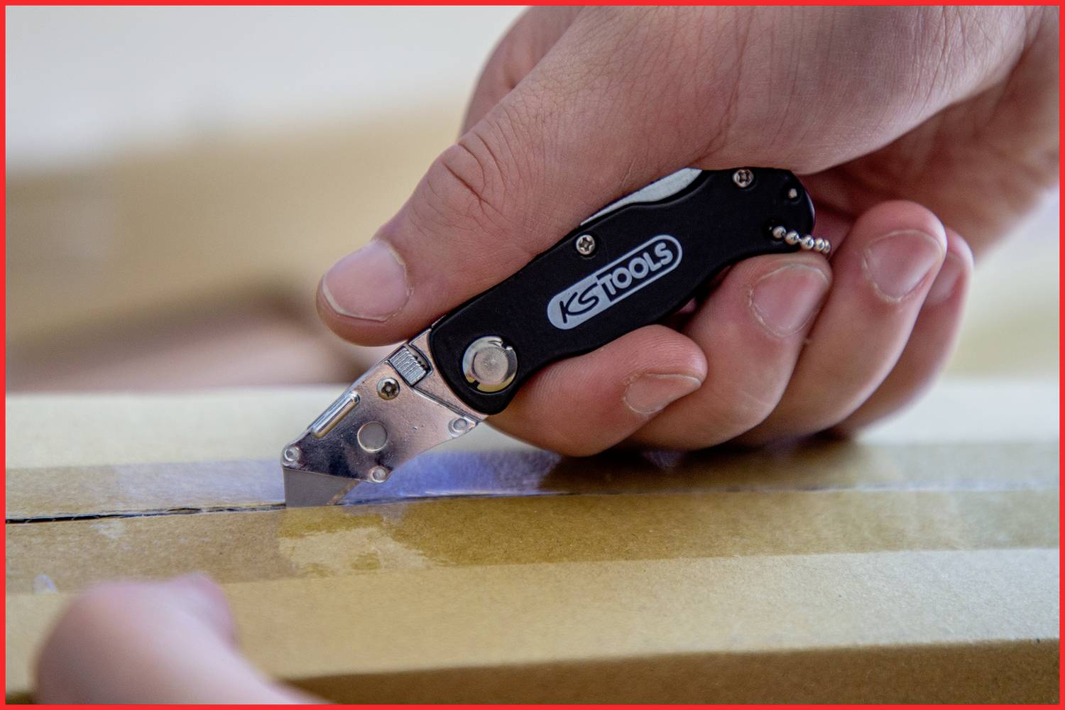 Une main utilise un couteau pliant noir pour couper du ruban adhésif sur un carton.
