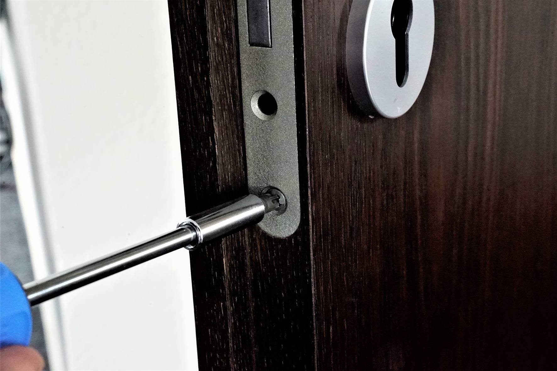 Un tournevis enfonce une vis dans une porte. La serrure de la porte présente une ouverture cylindrique argentée.