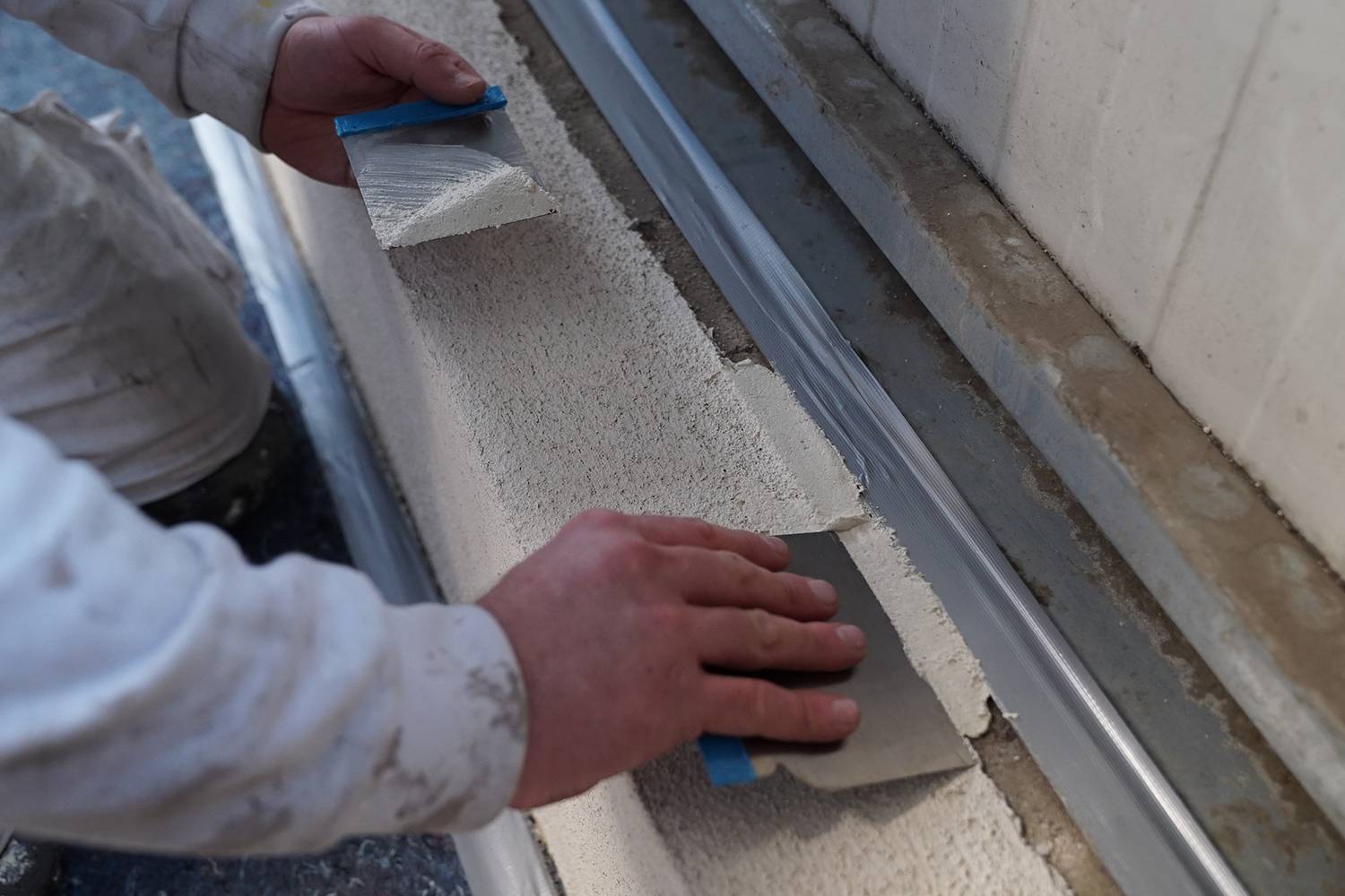 Une personne applique du mortier blanc sur un mur à l'aide d'une spatule. Le focus est mis sur les mains et la technique d'application.