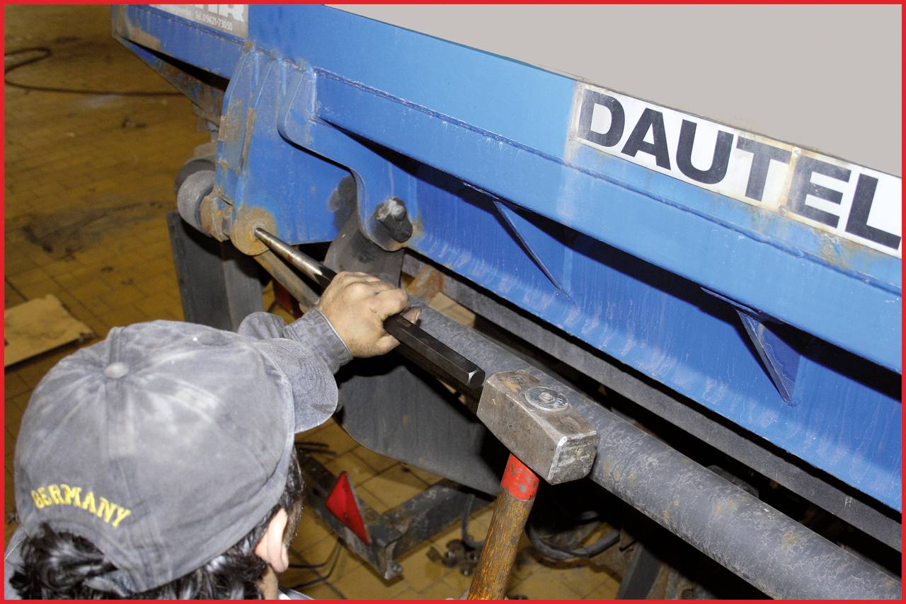 Une personne portant une casquette utilise un outil pour réparer ou ajuster la structure d'un camion bleu. Le mot 'DAUTEL' est visible.