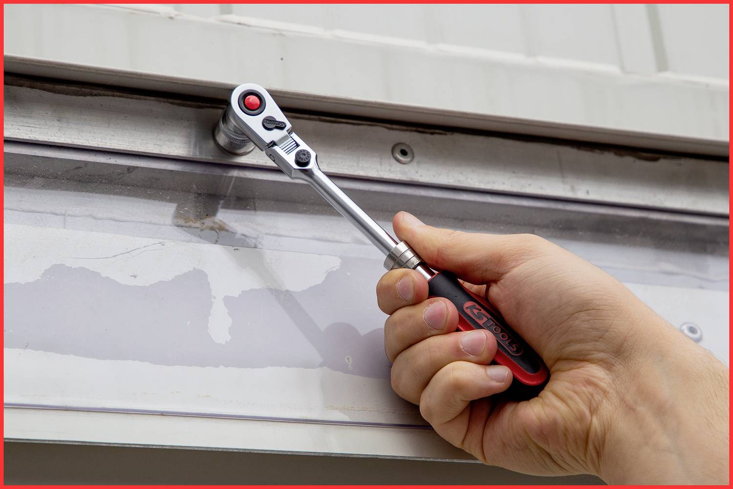 Une main tient une clé à cliquet et tourne une vis sur une plaque métallique.