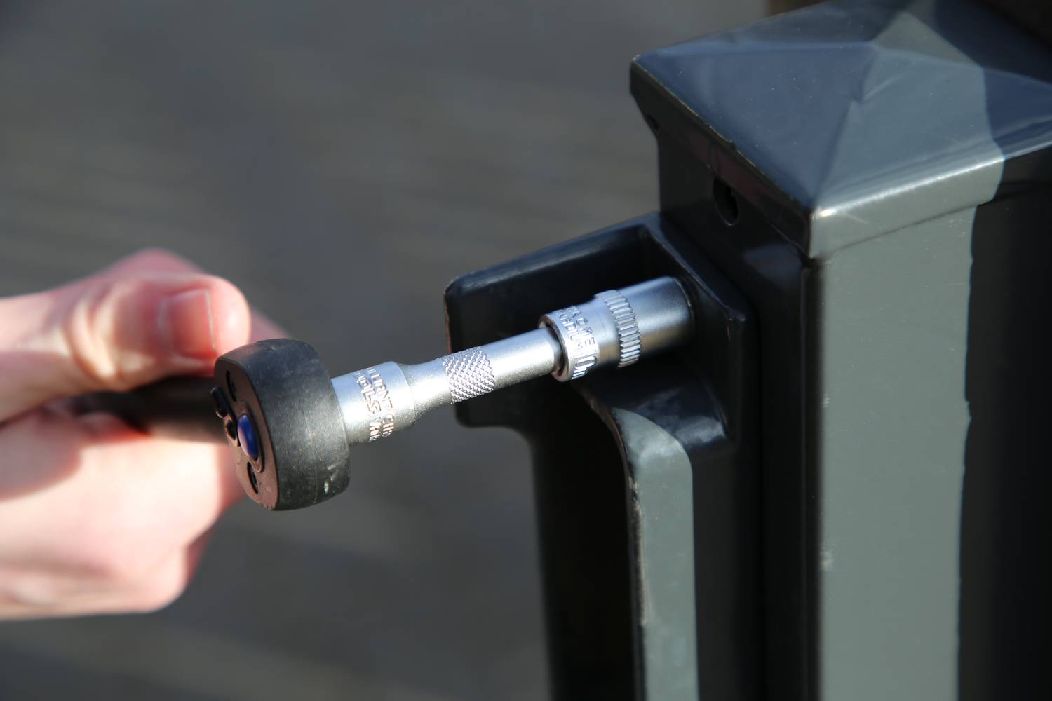 Une main utilise une clé dynamométrique pour serrer une vis sur une clôture métallique.