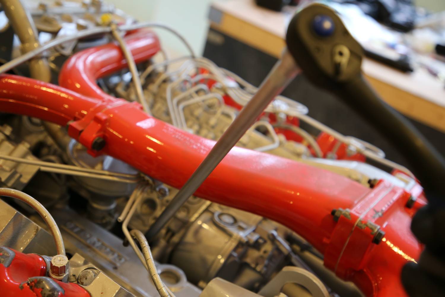 Moteur rouge au centre de l'attention, probablement un moteur marin, avec des outils et des vis. Atelier en arrière-plan. Thème : Mécanique/Maintenance.