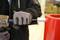 Une personne portant des gants de travail utilise un marteau pour frapper un outil métallique contre un objet rouge.