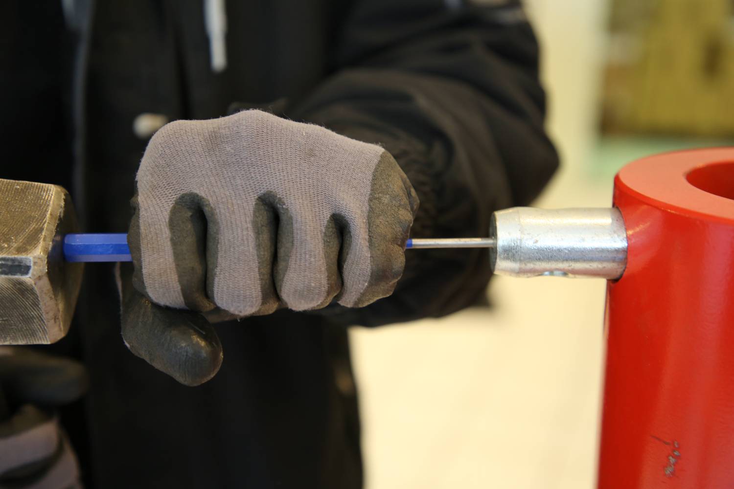 Une personne portant des gants de travail tend un fil bleu fin dans un dispositif rouge à l'aide d'un outil.