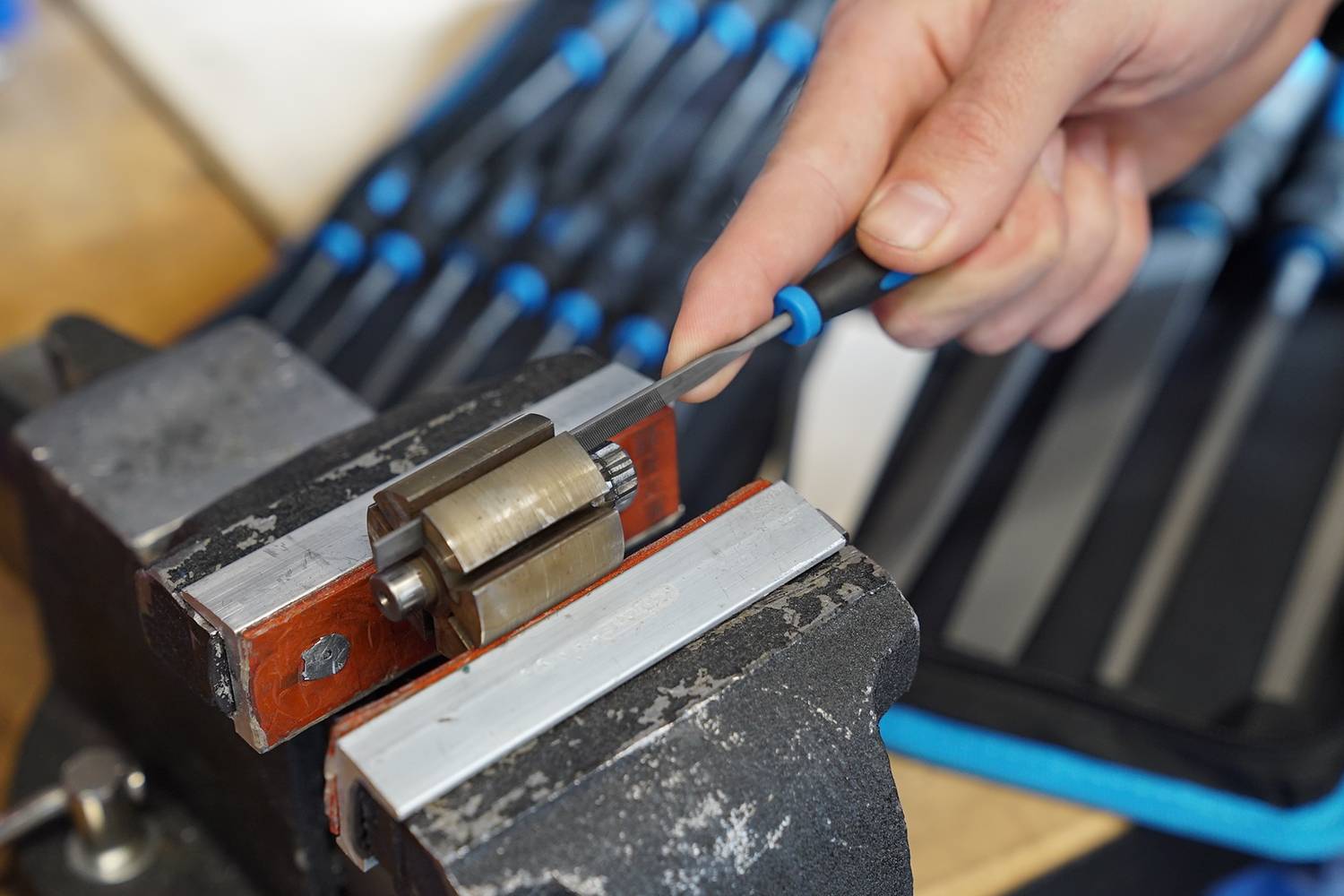 Une personne affûte un tournevis sur une machine, plusieurs outils étant visibles en arrière-plan.