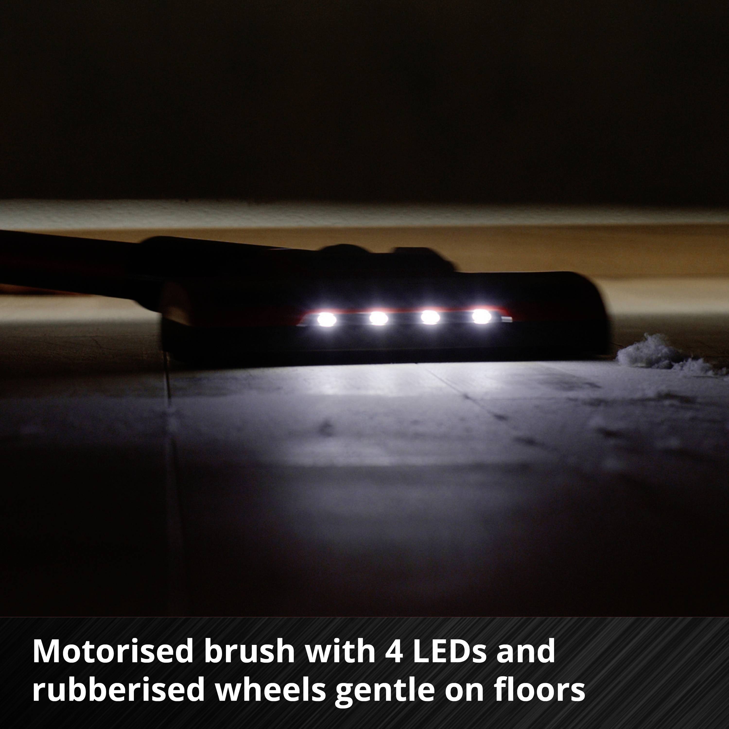 Brosse motorisée avec 4 LED et roues en caoutchouc ménageant le sol. Une buse d'aspirateur avec des lumières LED luminescentes sur un sol sombre.