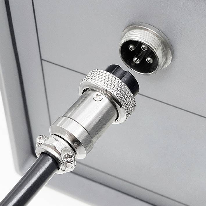 Une fiche ronde argentée est branchée sur un connecteur correspondant sur un appareil gris.