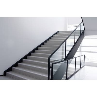 Cage d'escalier avec des marches blanches et une rampe noire moderne, menant à une zone de fenêtres baignée de lumière.