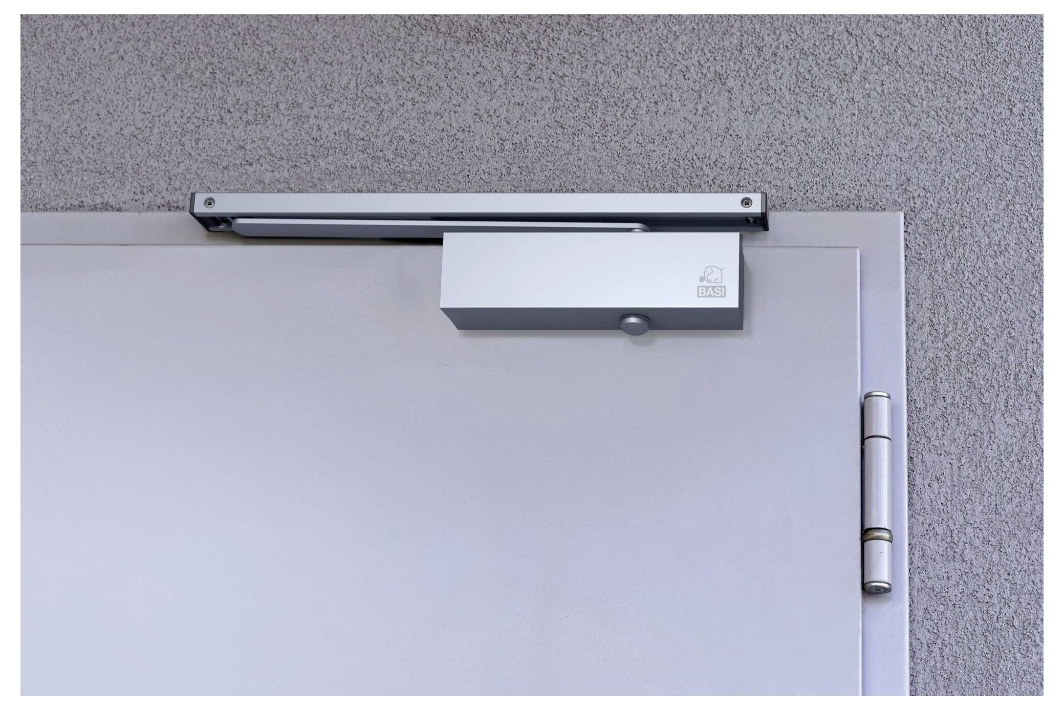 Un ferme-porte argenté installé en haut d'une porte grise, contre un mur texturé.