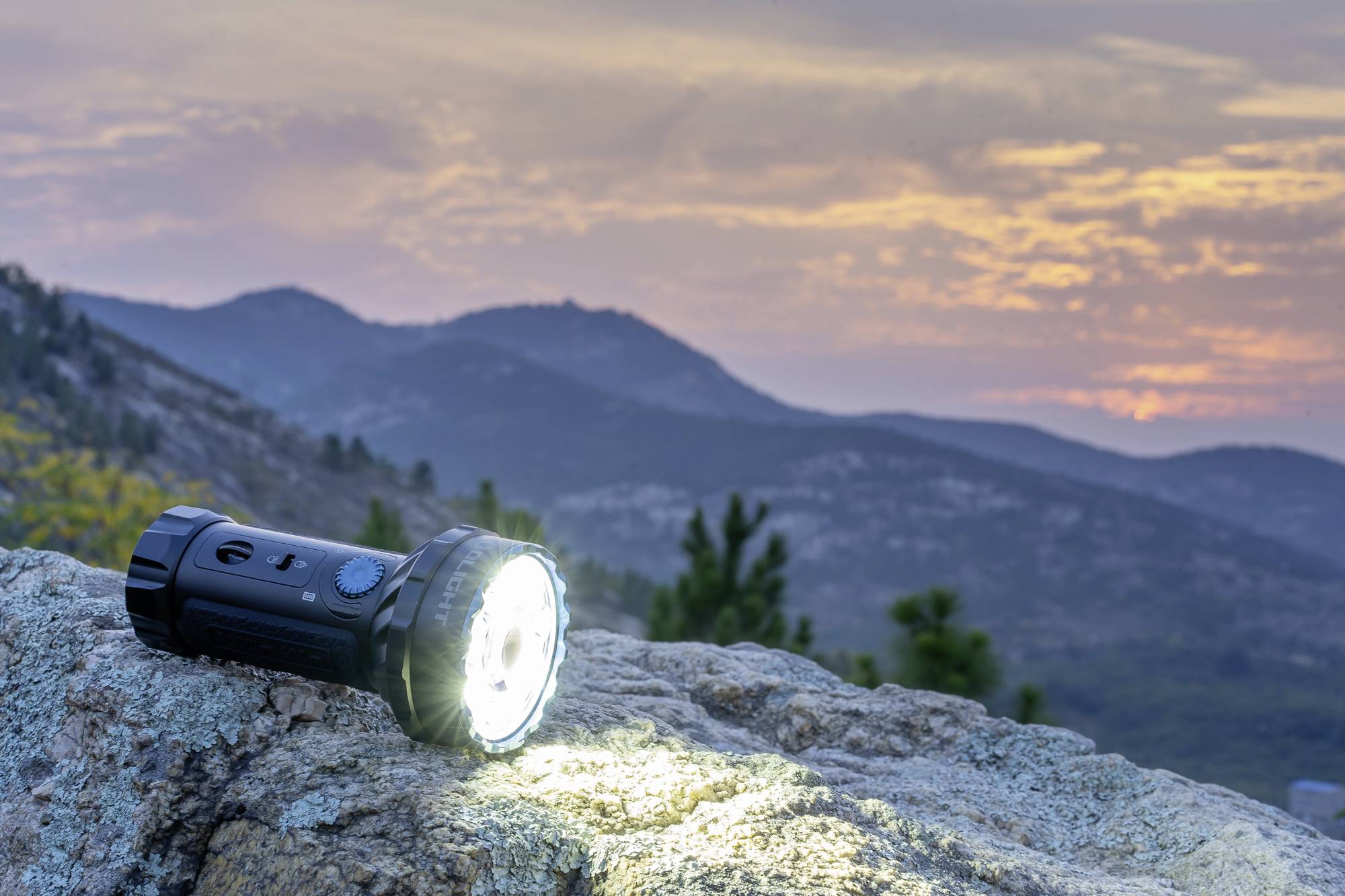 Une lampe de poche brille sur une pierre au crépuscule, avec des montagnes en arrière-plan. Le ciel présente un mélange d'orange et de violet.