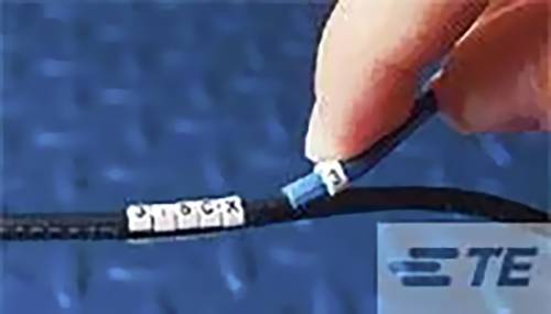 L'image montre une main qui tient un câble avec un connecteur bleu. Sur le câble se trouvent des étiquettes blanches avec des marquages.
