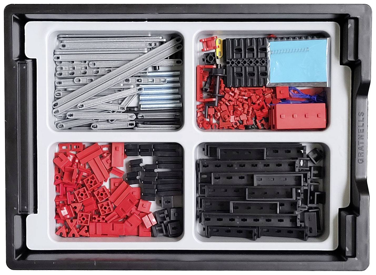 Un bac ouvert contenant des pièces LEGO Technic triées en rouge et noir, ainsi que des axes argentés et des petites pièces bleues et rouges.