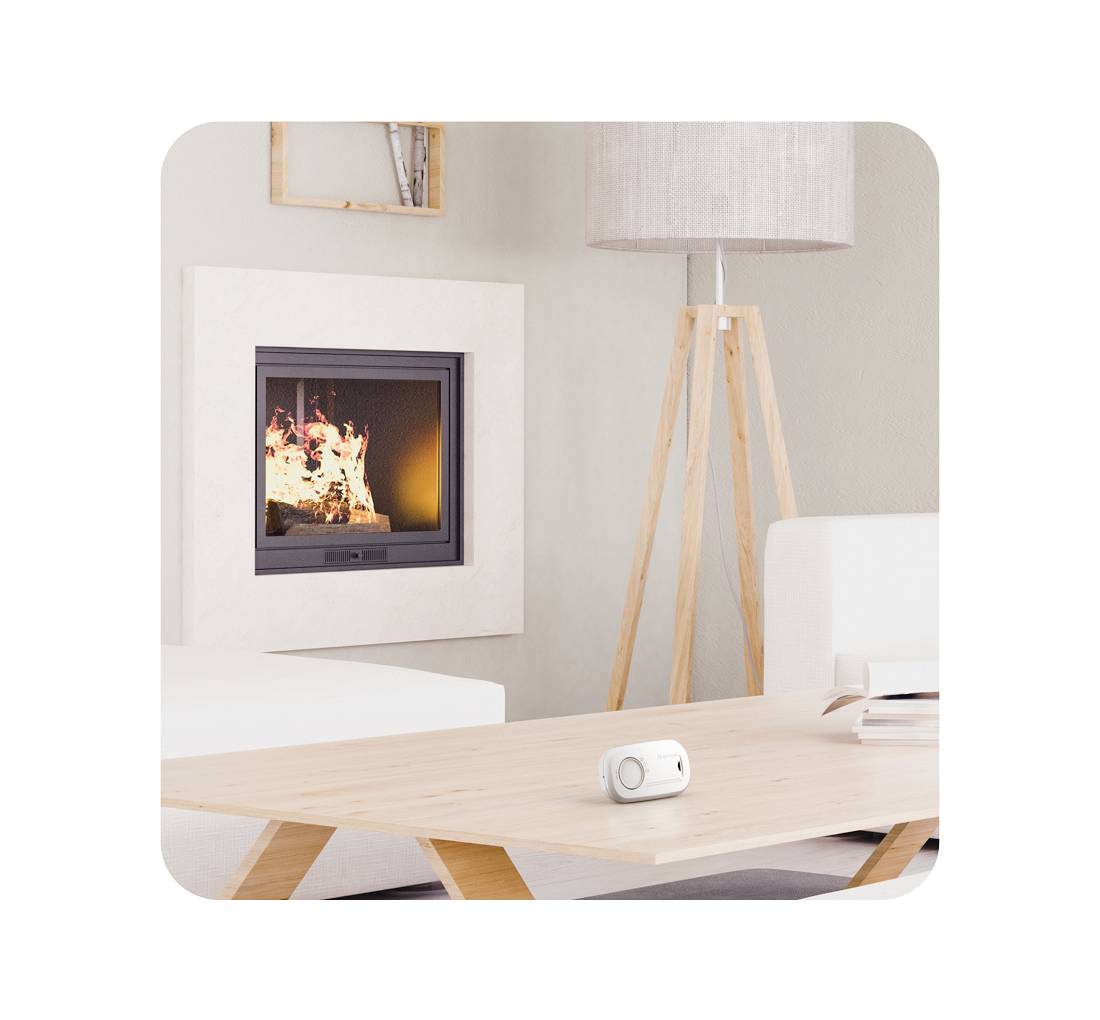 Un salon moderne avec une cheminée allumée, un canapé blanc, une table en bois et un lampadaire. Un petit appareil blanc est posé sur la table.