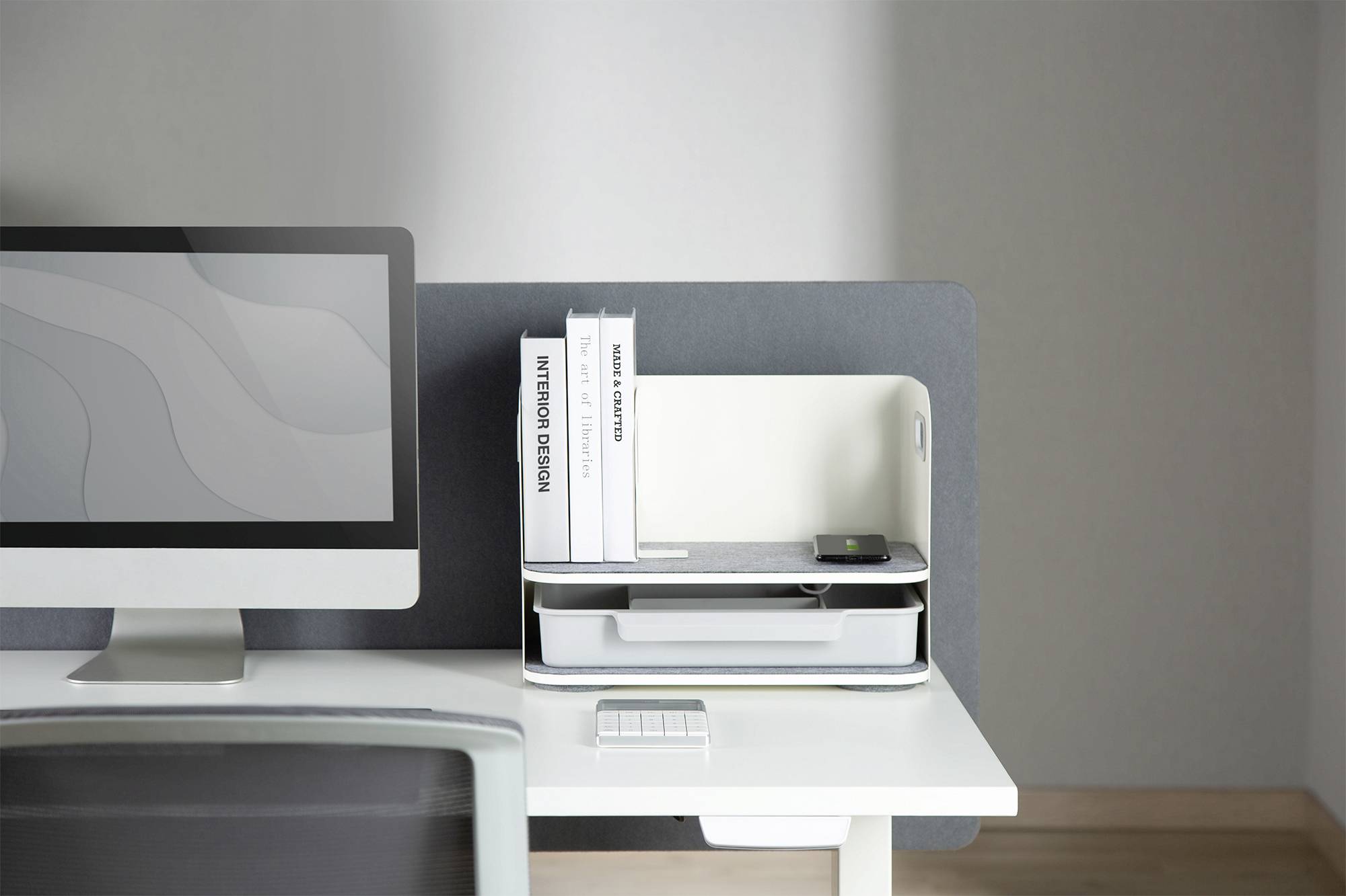 Un bureau moderne avec un écran d'ordinateur ; à côté se trouvent des livres et une petite boîte de rangement. Design minimaliste.