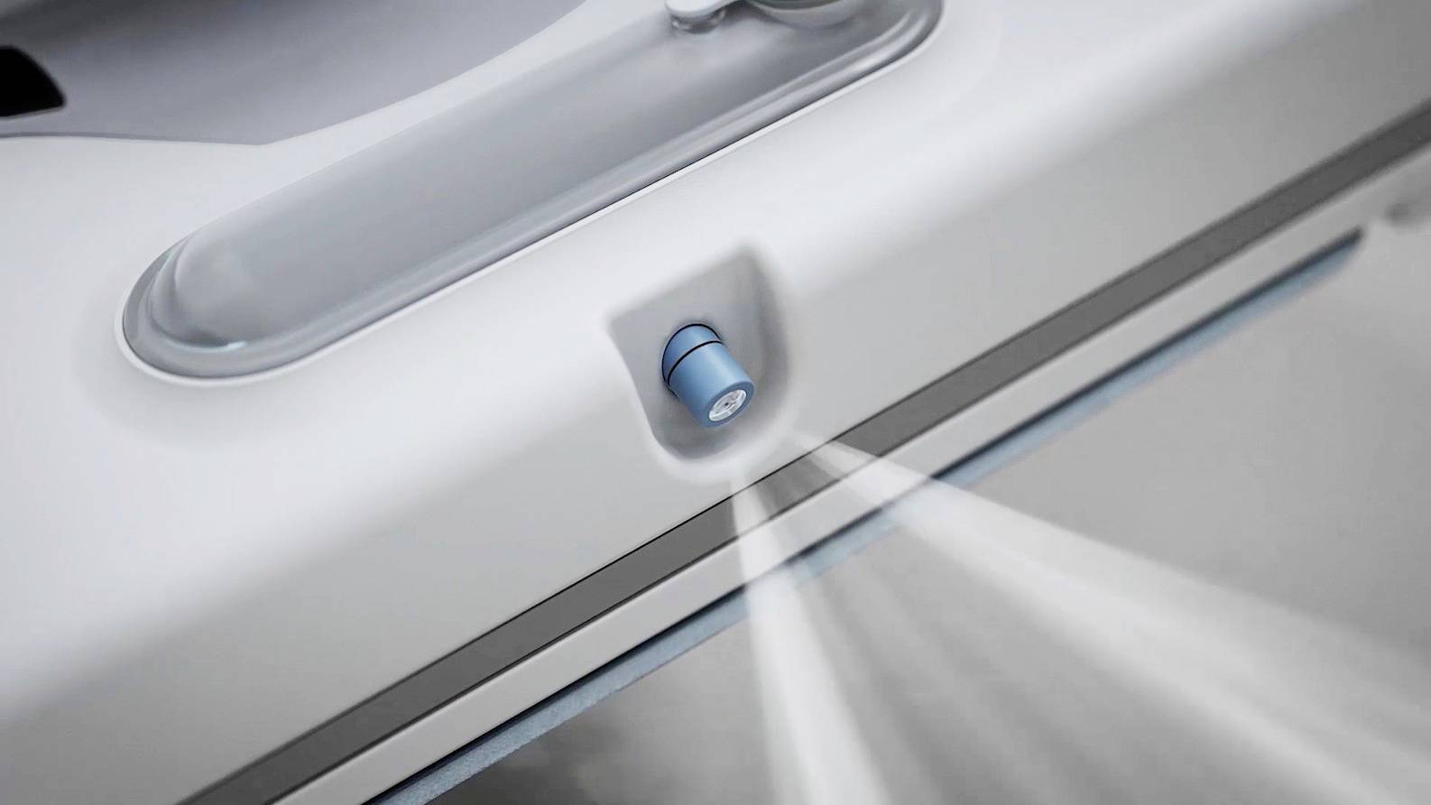 Un aspirateur pulvérise un liquide de nettoyage à travers une buse bleue sur une surface pour la nettoyer.