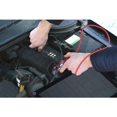 Une personne répare une batterie de voiture à l'aide de câbles de démarrage. Les mains connectent le câble rouge à la borne de démarrage du véhicule.
