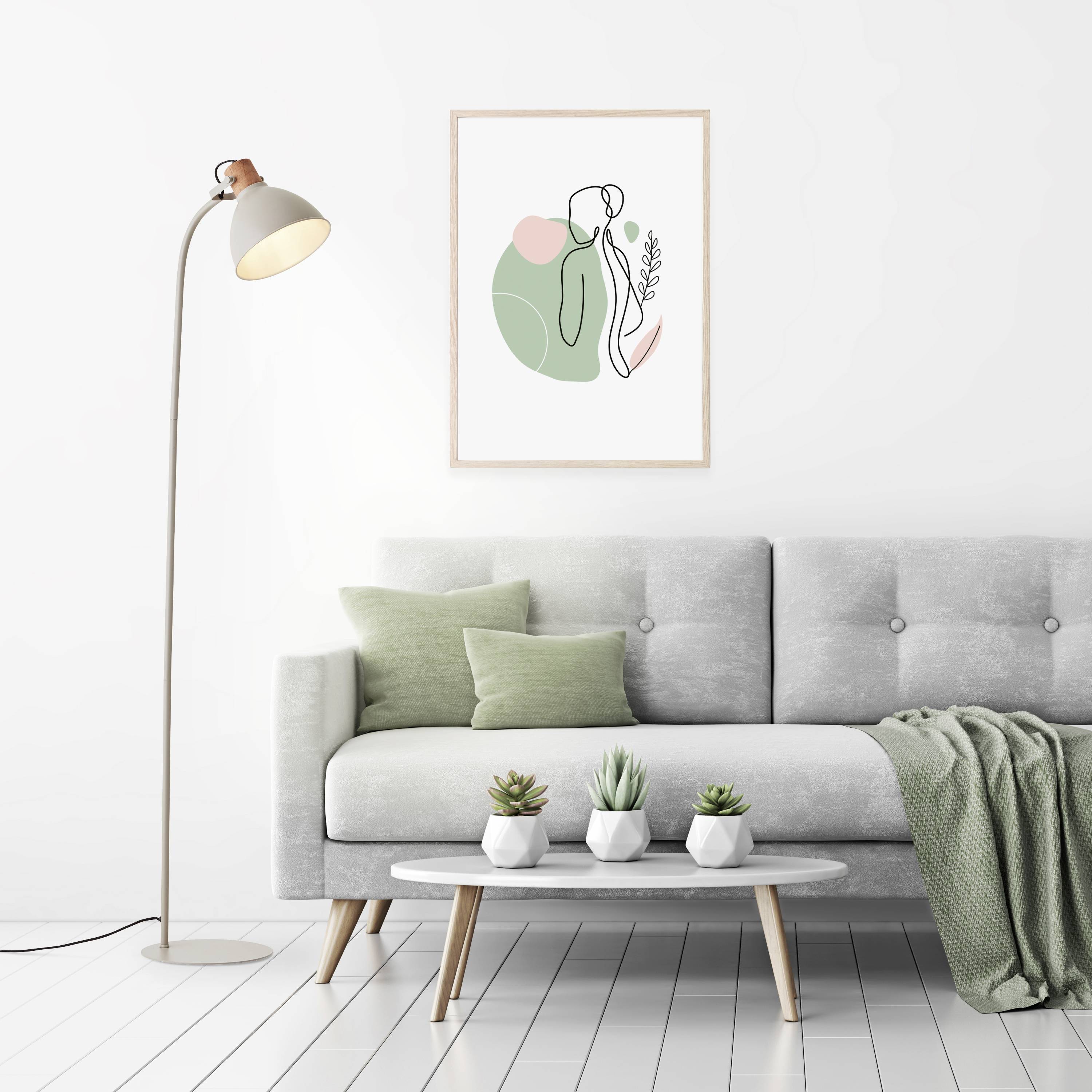 Salon moderne avec canapé gris, coussin vert et couverture, table basse en bois clair, lampadaire et tableau abstrait mural.